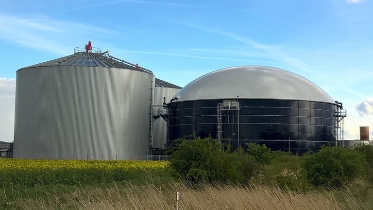 Biogasbehälter hinter Wiese unter blauem Himmel